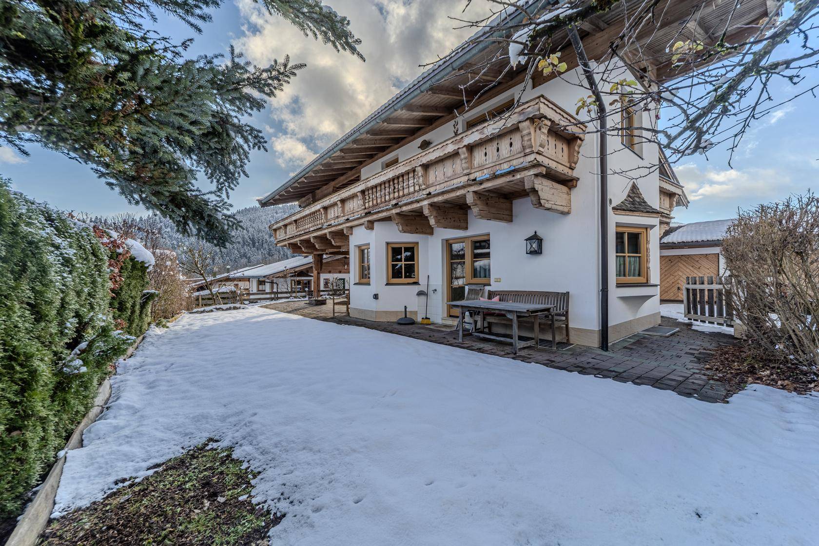 Traditionelles Chalet mit Holzbalkonen und verschneitem Gartenbereich in alpiner Umgebung.