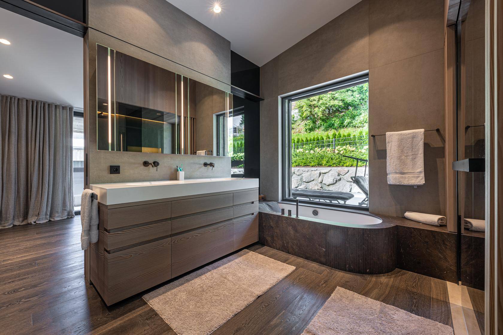 Modernes Badezimmer mit Doppelwaschbecken, Badewanne am Fenster und Holzboden.