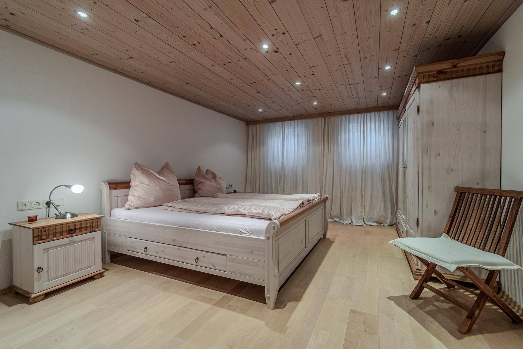 Helles Schlafzimmer mit Holzboden, Holzdecke und traditionellen weißen Holzmöbeln.