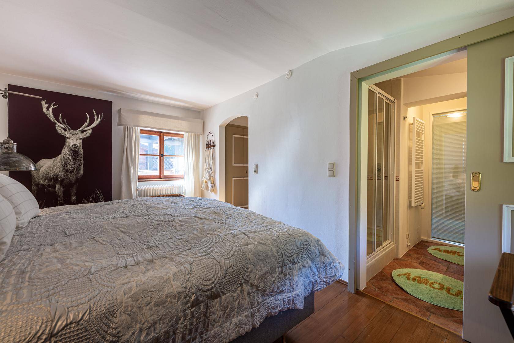 Schlafzimmer mit Holzboden, Hirschmotiv an der Wand und direktem Zugang zur Dusche.