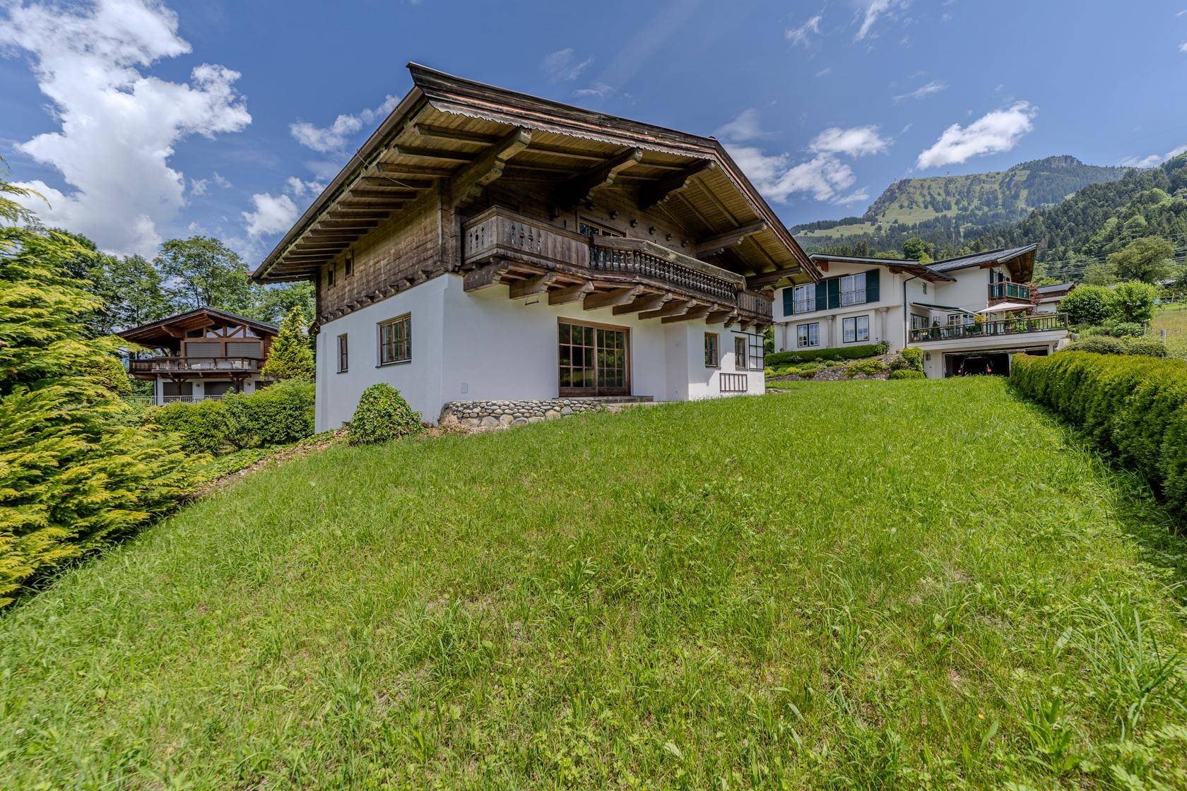 Charmantes Haus im Alpenstil auf einem Hügel gelegen, umgeben von üppigem Grün und Bergen.