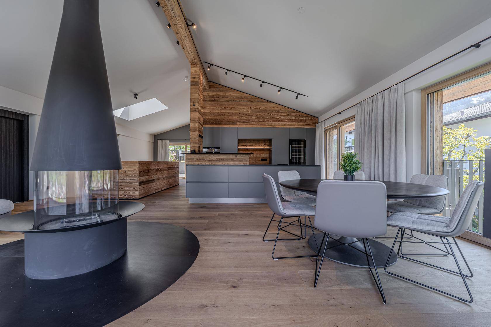 Heller Essbereich mit modernem Kamin und offener Küche in Grau und Holz.