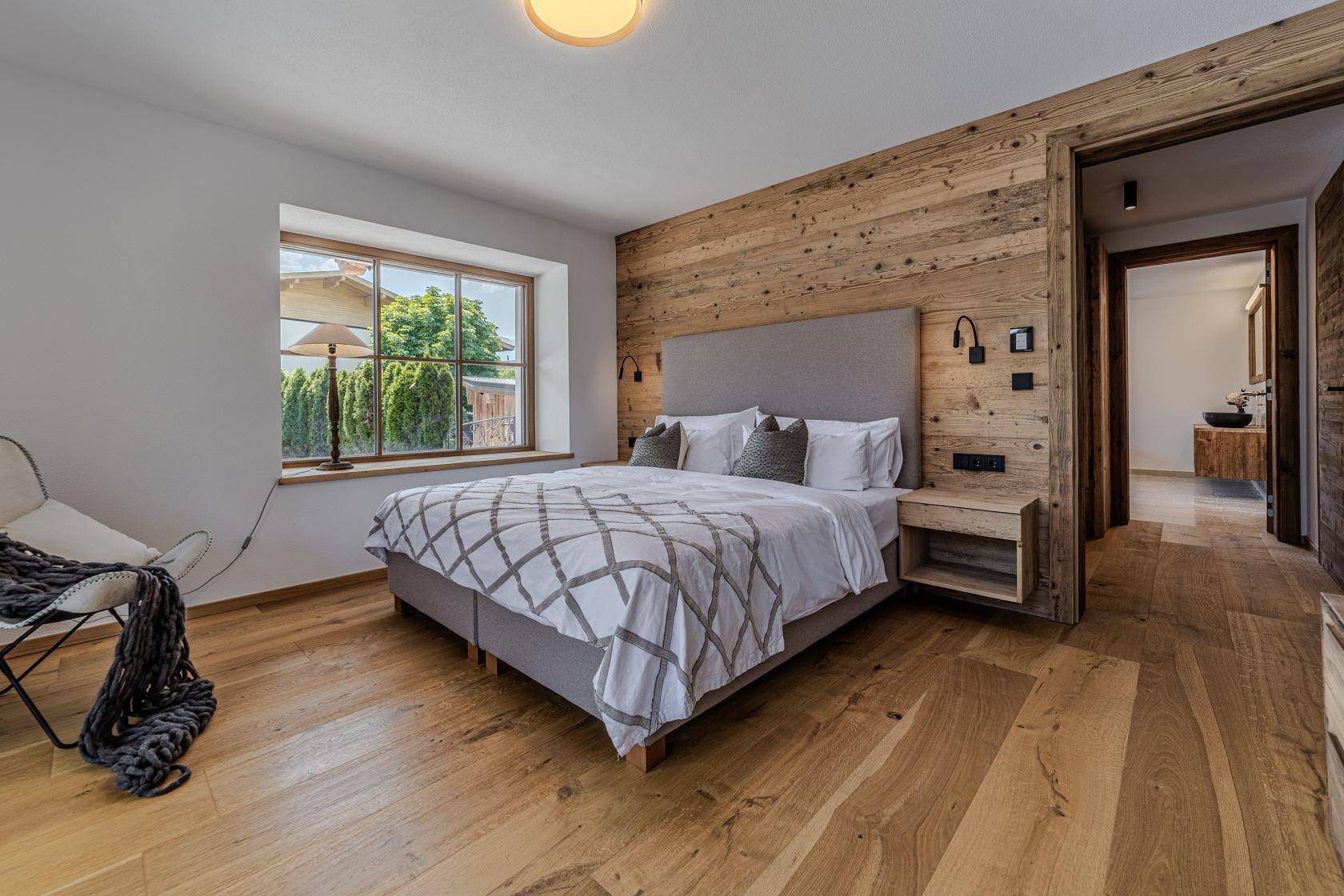 Gemütliches Schlafzimmer mit Holzakzentwand, Holzboden und direktem Zugang zu einem modernen Badezimmer.
