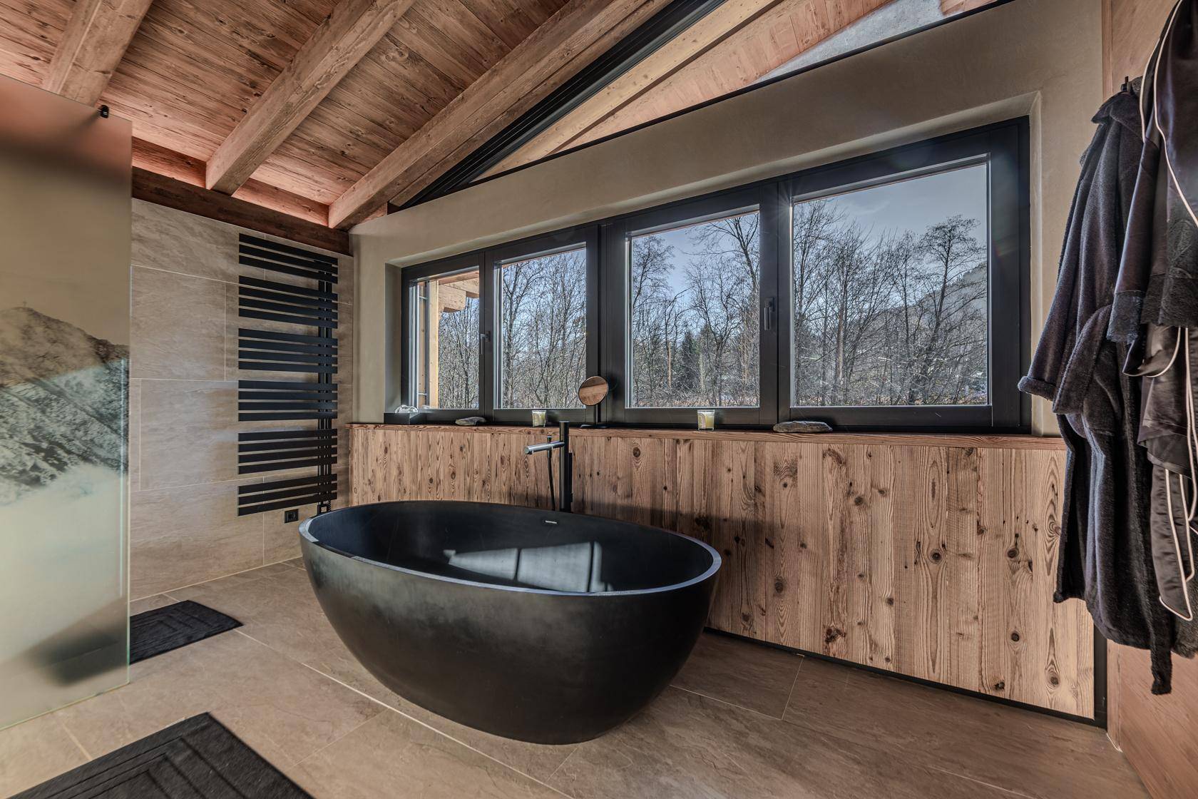 Modernes Badezimmer mit freistehender Badewanne, Holzelementen und großem Fenster mit Waldblick.