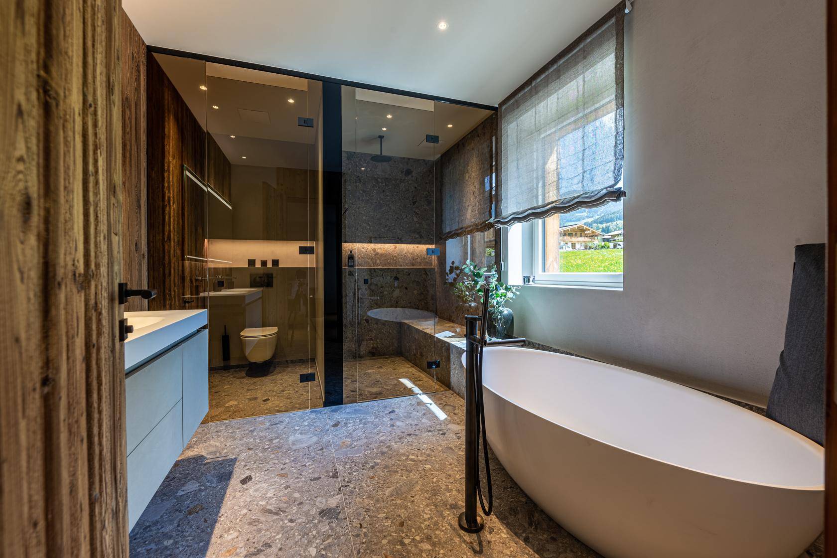 Modernes Badezimmer mit freistehender Badewanne, begehbarer Dusche und Fenster mit Blick ins Grüne.