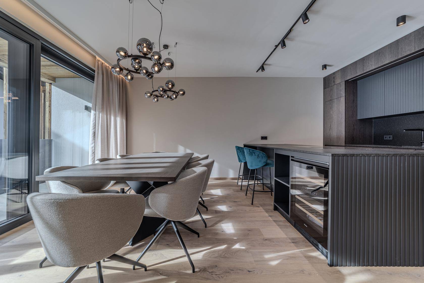 Eleganter Essbereich mit Holztisch und offener Küche, ausgestattet mit einem Weinkühler und großen Fenstern.