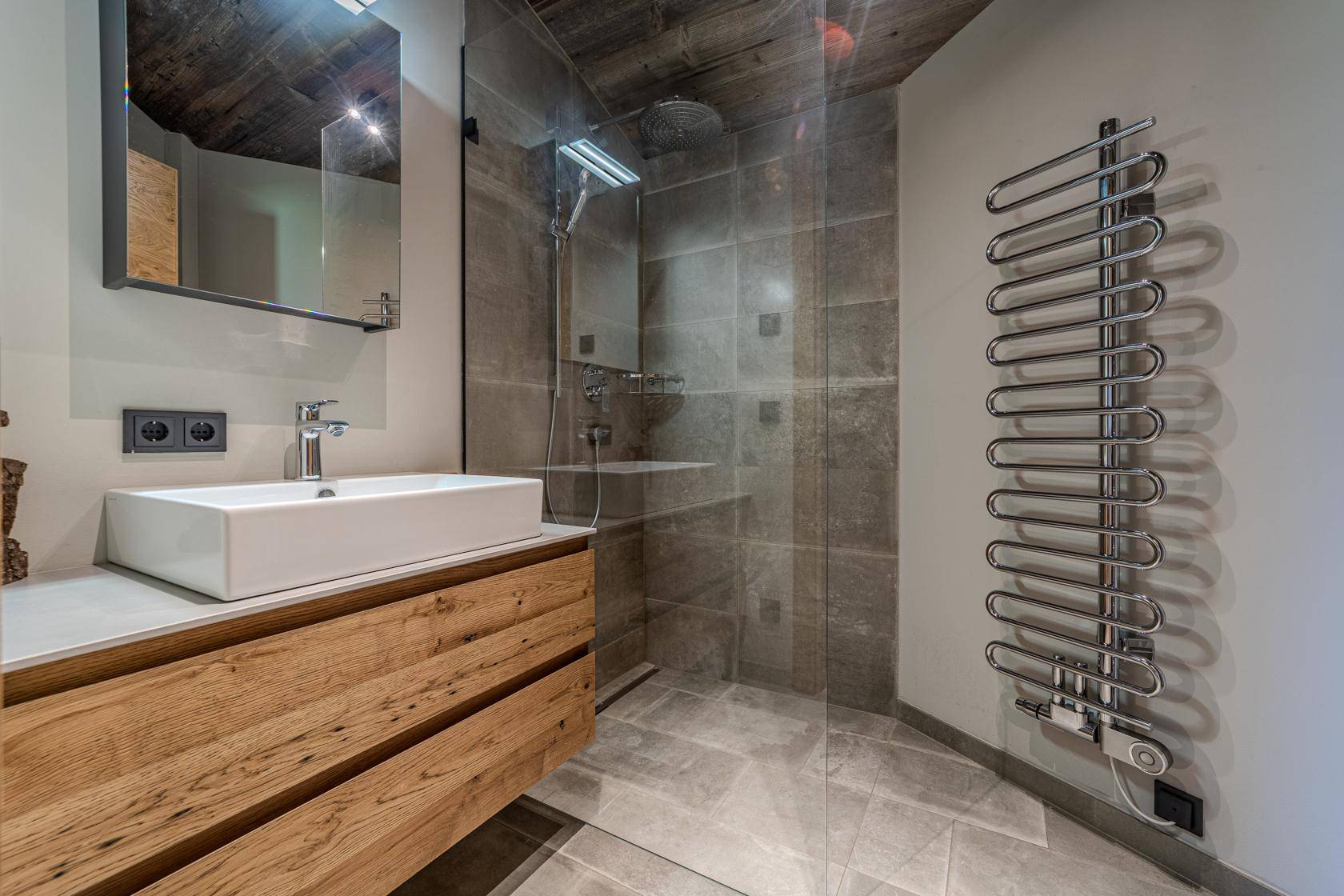 Modernes Badezimmer mit Waschtisch, begehbarer Dusche und beheiztem Handtuchhalter, in Grautönen gehalten.