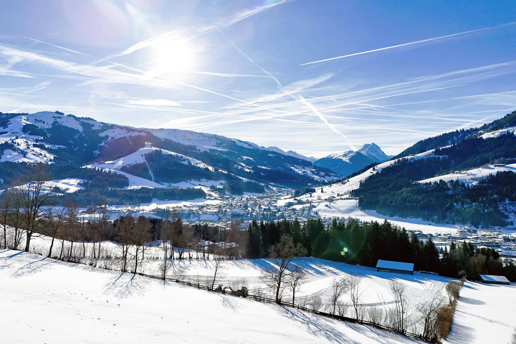 Panoramablick über eine weite, schneebedeckte Berglandschaft mit Tälern und Wäldern.