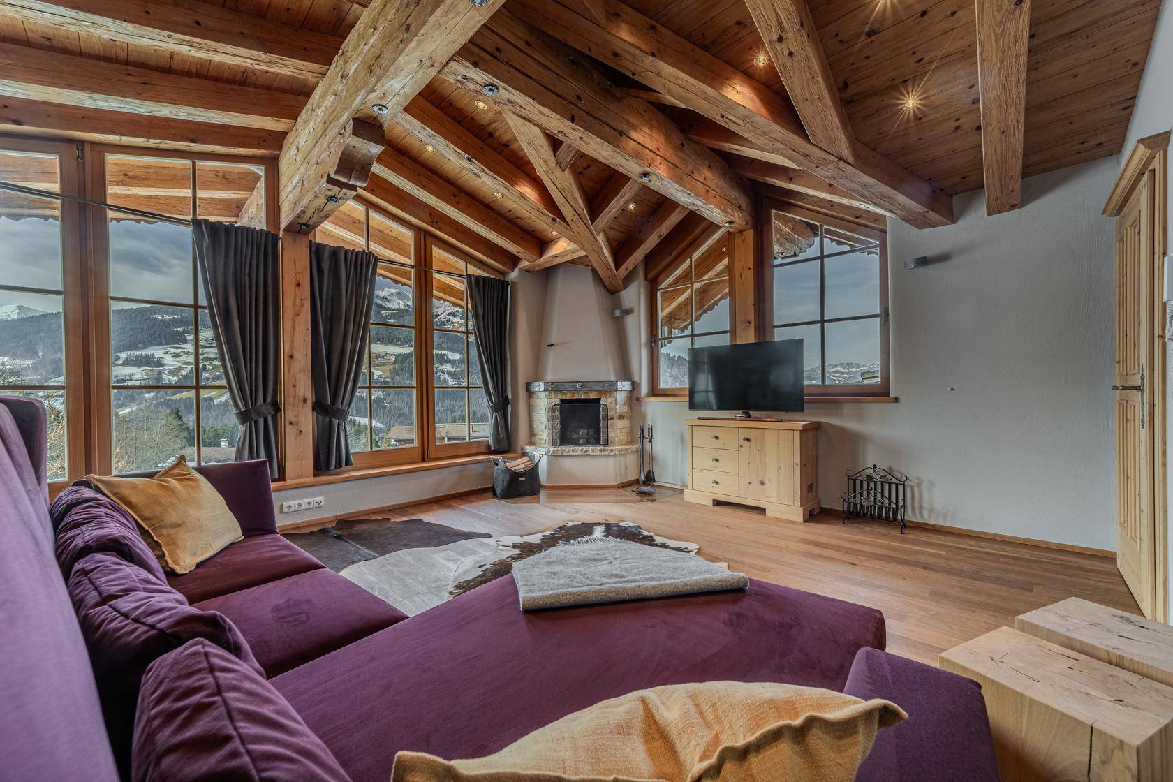 Gemütliches Wohnzimmer mit Holzbalkendecke, Kamin und atemberaubendem Bergblick durch große Fenster.