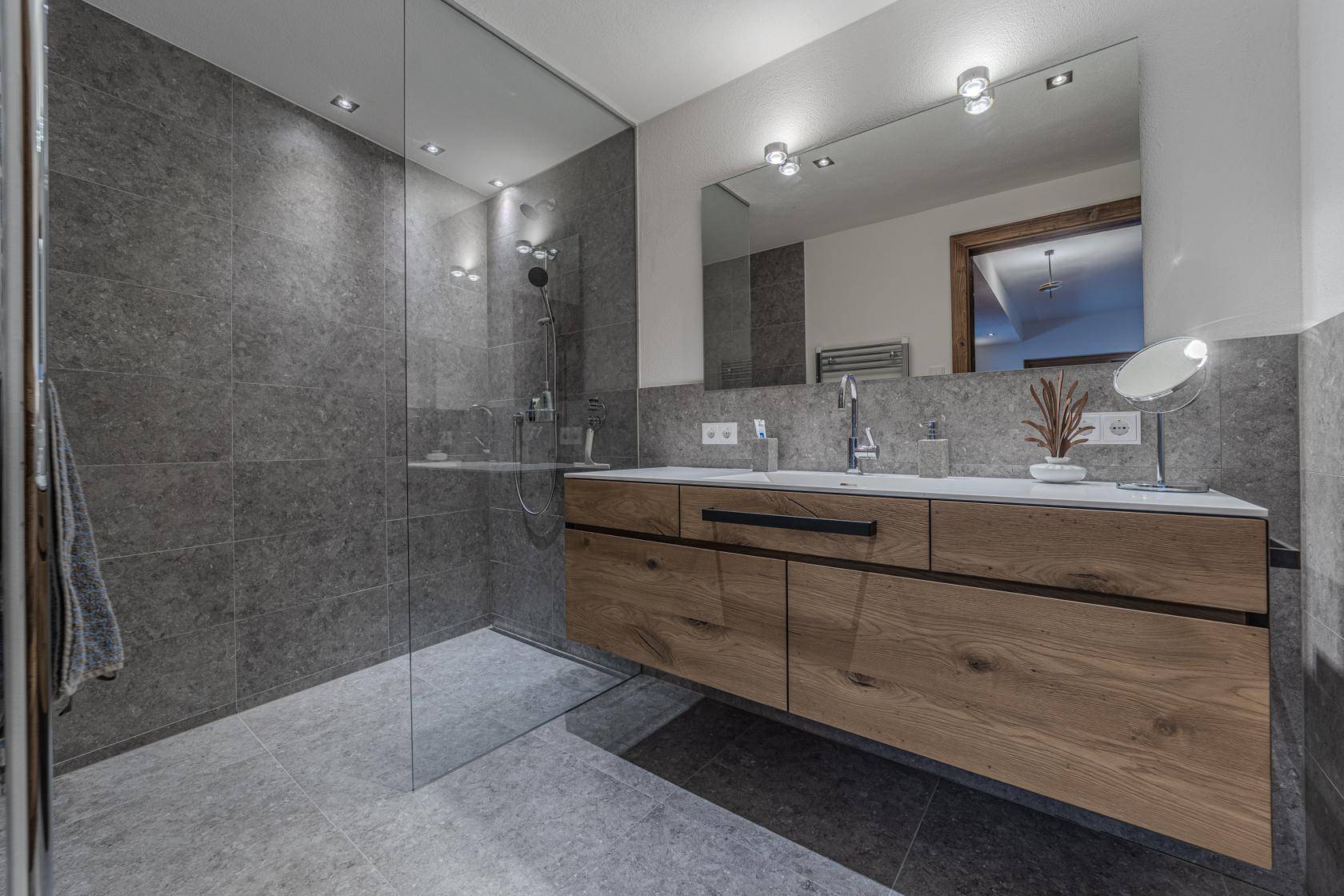 Modernes Badezimmer mit großer begehbarer Dusche, Doppelwaschbecken und eleganten grauen Fliesen.
