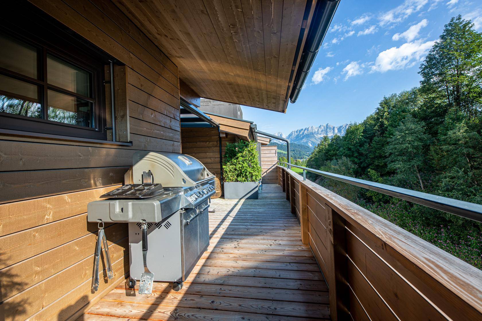 Langer Holzbalkon mit Grillstation und atemberaubendem Blick auf die umliegenden Berge.