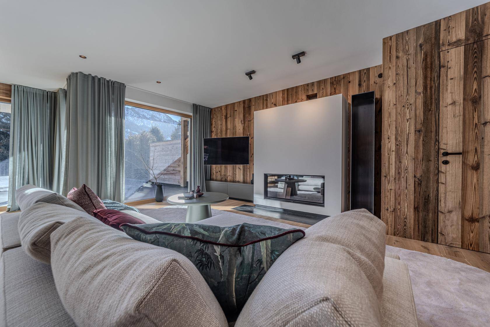 Gemütliches Wohnzimmer mit modernem Kamin, Holzwänden und Blick auf die verschneite Natur.