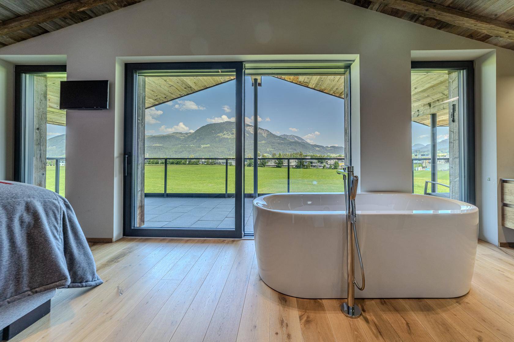 Schlafzimmer mit freistehender Badewanne, Holzboden und Zugang zu einer Terrasse mit Bergblick.