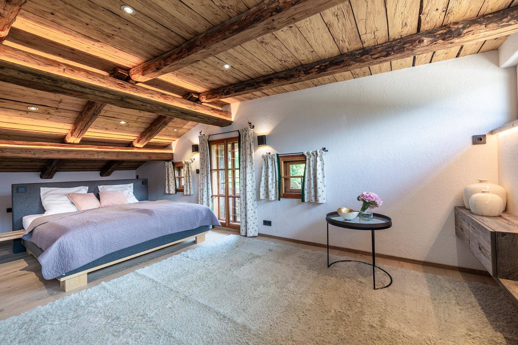Helles Schlafzimmer im Dachgeschoss mit Holzbalken und gemütlichem Teppichboden.