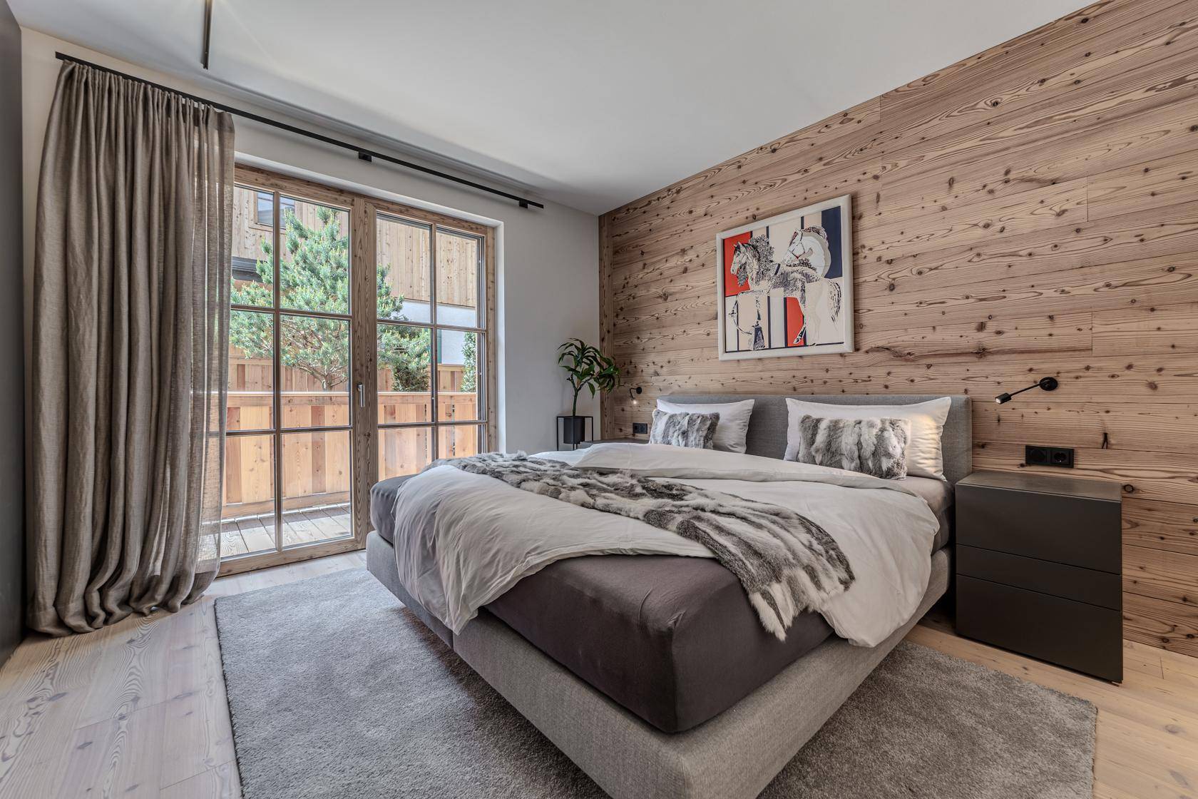 Helles Schlafzimmer mit Holzwand, großem Doppelbett und direktem Zugang zu einer Terrasse.