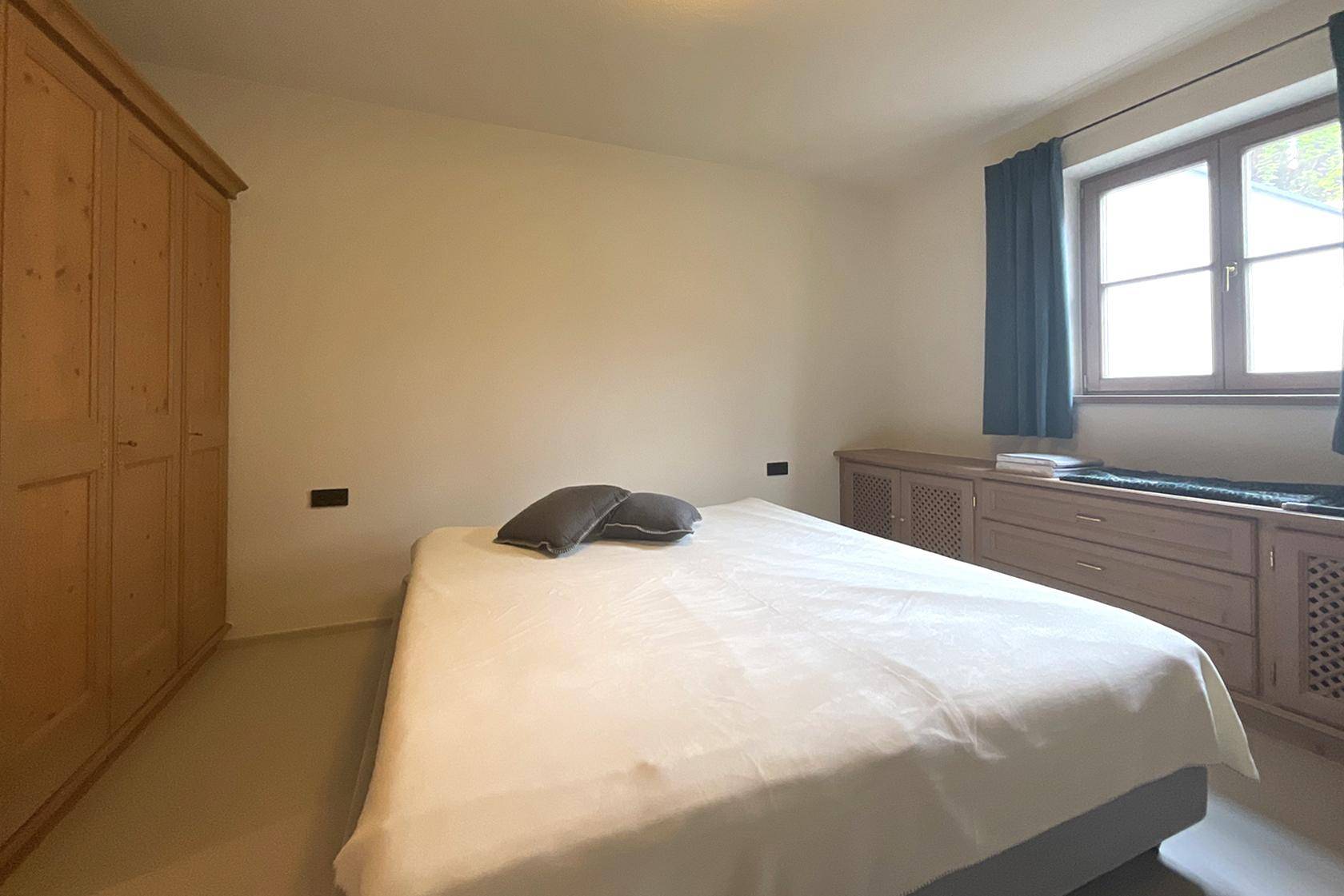 Helles Schlafzimmer mit Holzkleiderschrank, Doppelbett und Fenster mit Ausblick.