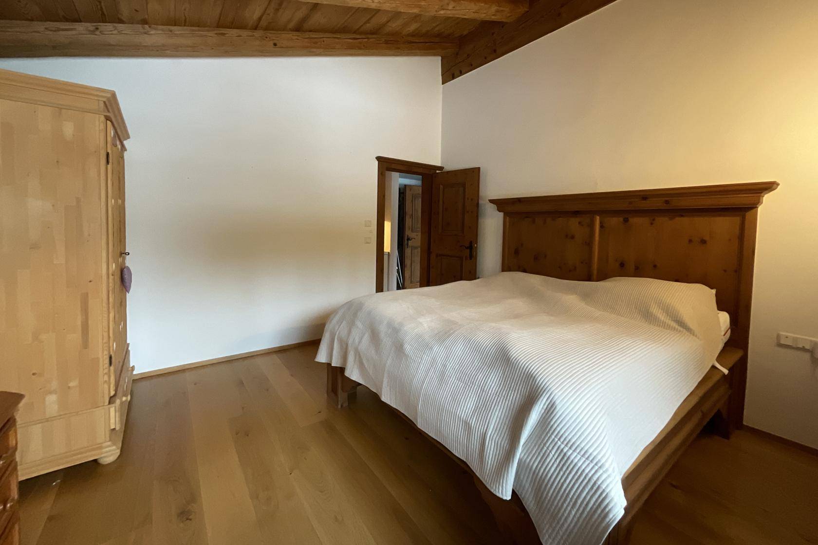 Schlafzimmer mit Holzbalkendecke, Doppelbett und traditionellem Holzschrank.