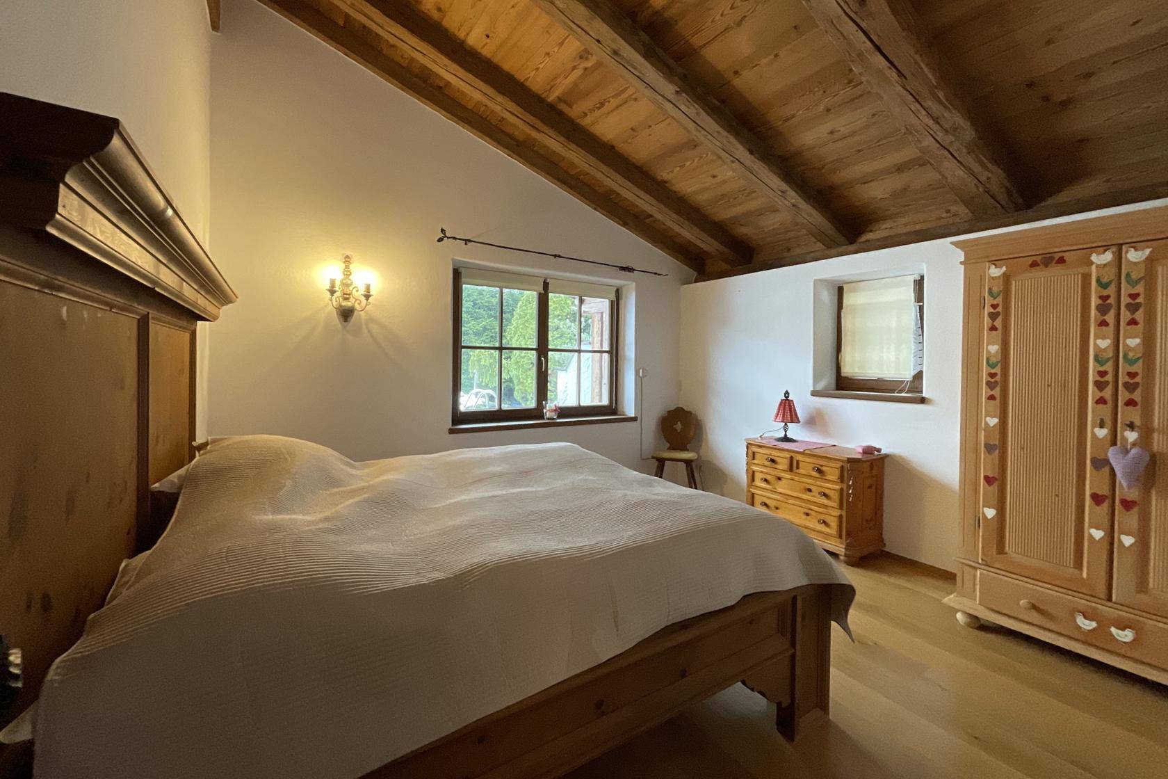 Gemütliches Schlafzimmer mit Holzbalkendecke, Doppelbett und Blick ins Grüne.