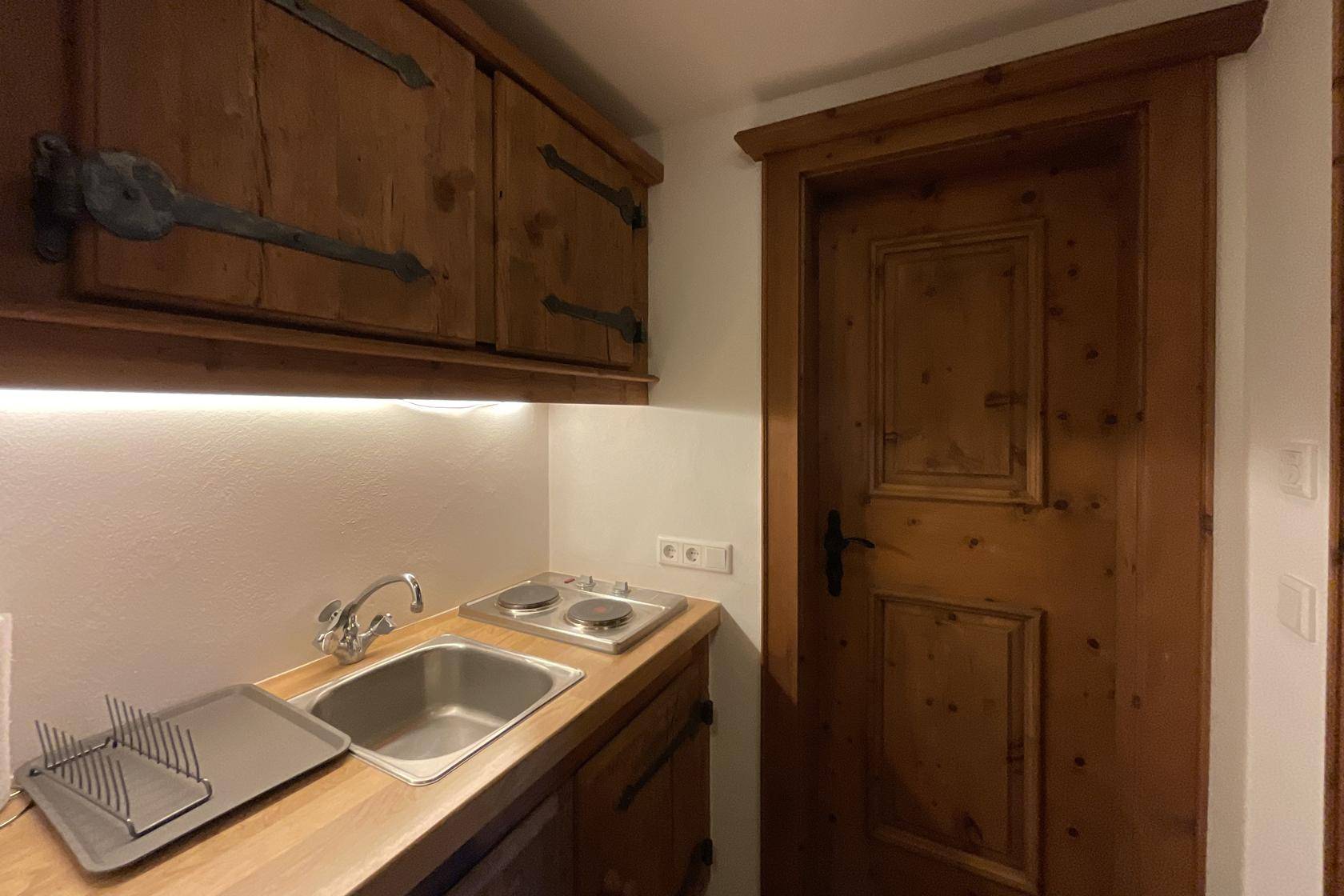 Kleine Küchenzeile mit Spüle, Kochplatten und rustikalen Holzschränken.