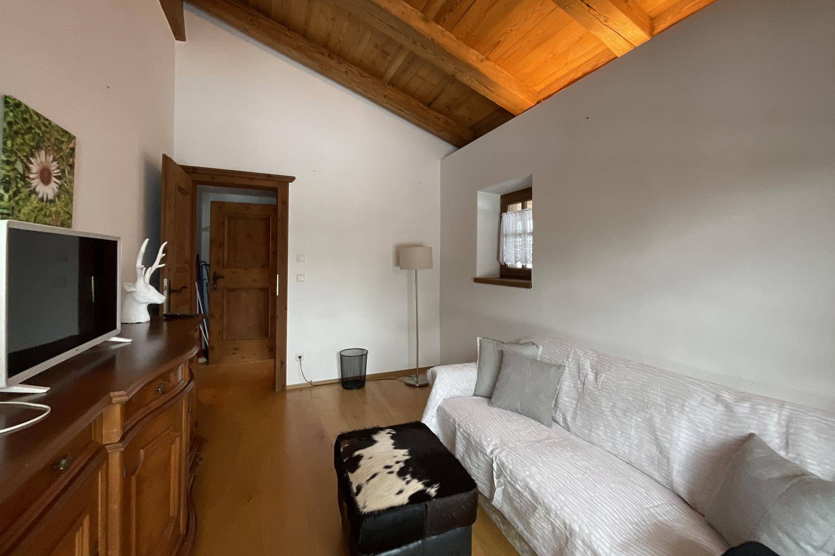 Helles Wohnzimmer mit Holzbalkendecke, Sofa und traditionellen Holzmöbeln.