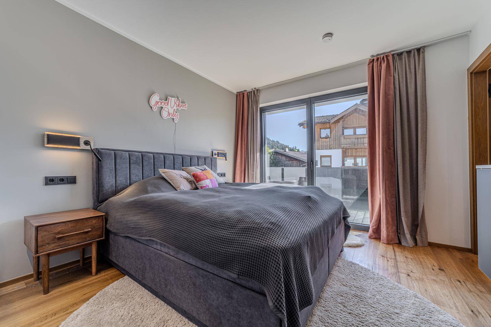 Helles Schlafzimmer mit Doppelbett, Holzboden und direktem Zugang zu einem Außenbereich.