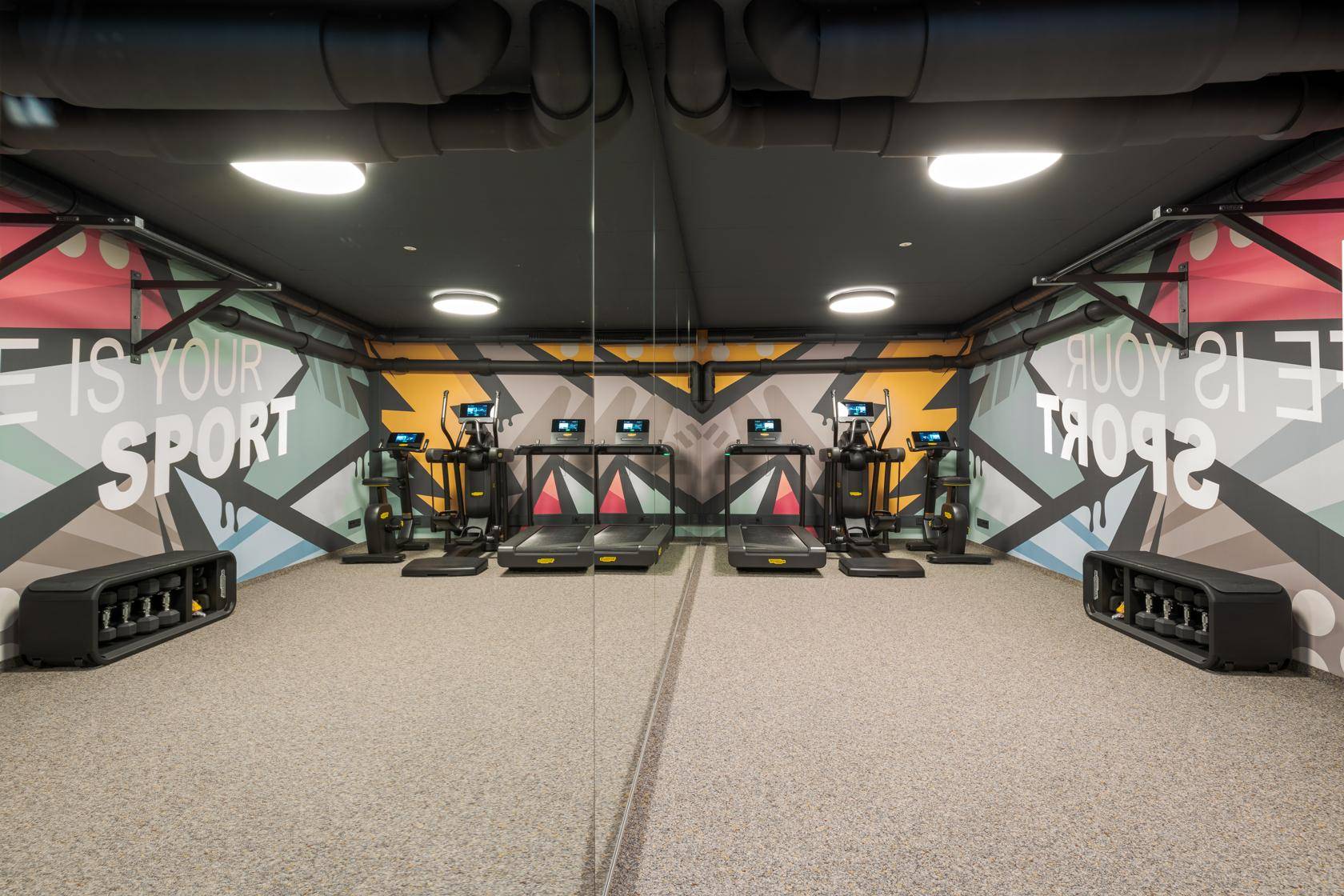 Moderner Fitnessraum mit verschiedenen Trainingsgeräten und farbenfroher Wandgestaltung.