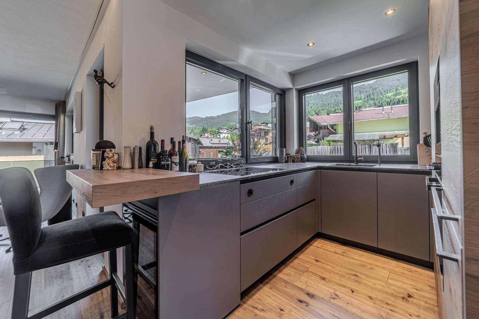 Moderne Küche mit grauen Schränken, Holz-Frühstücksbar und weitem Blick auf die umliegende Landschaft.