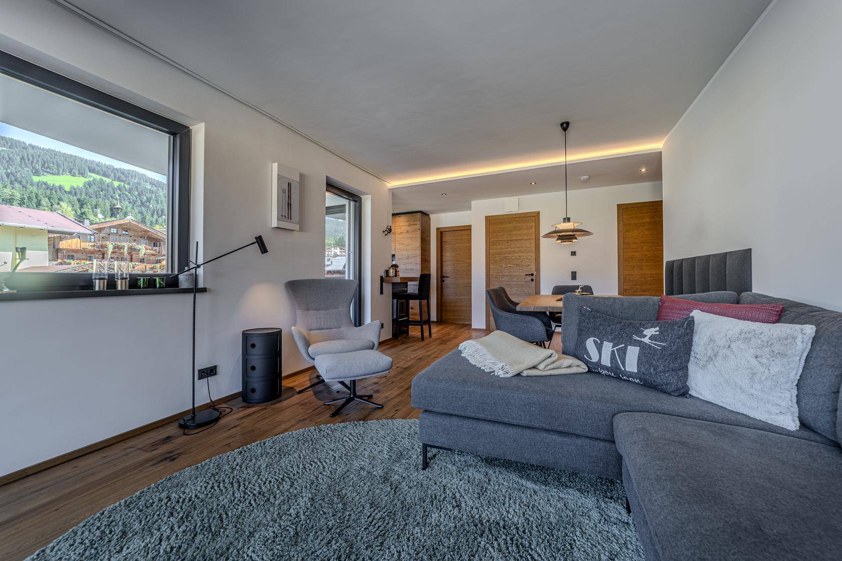 Gemütlicher Wohnbereich mit modernem Sofa, Holzboden und Blick auf die grüne Berglandschaft.