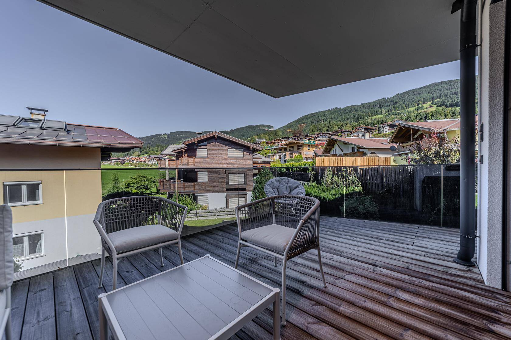 Sonniger Balkon mit Holzboden und bequemen Sitzgelegenheiten, bietet einen weiten Blick ins Grüne.