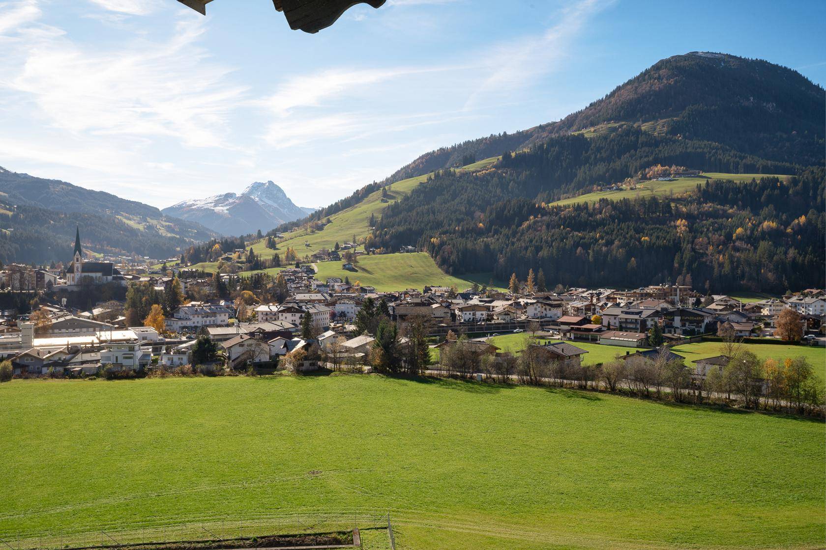 Weitläufiger Blick über ein malerisches Tal mit einem Dorf und schneebedeckten Bergen im Hintergrund.