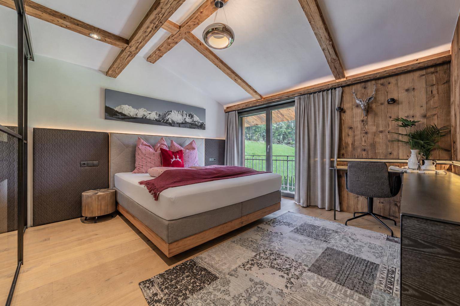 Geräumiges Schlafzimmer mit Holzbalken, Schreibtisch und Zugang zu einem Balkon.