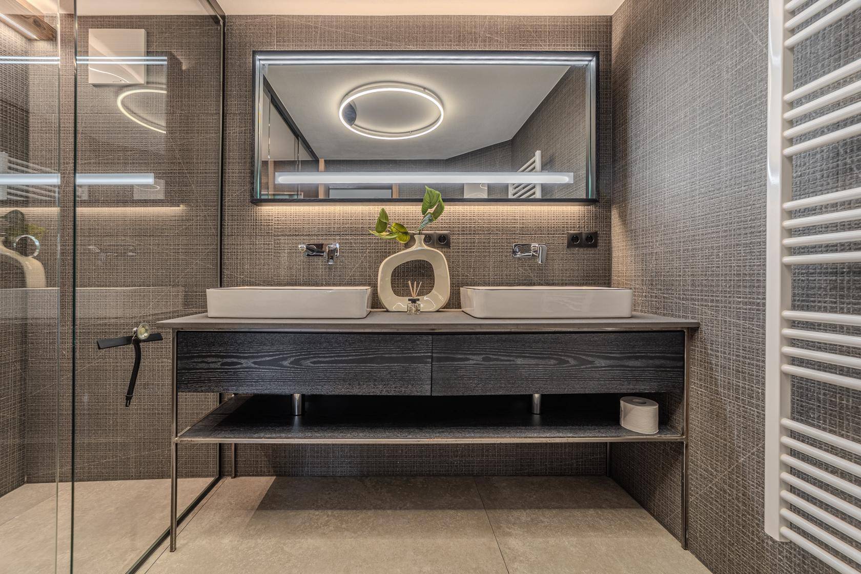 Modernes Badezimmer mit Doppelwaschbecken, beleuchtetem Spiegel und begehbarer Dusche.