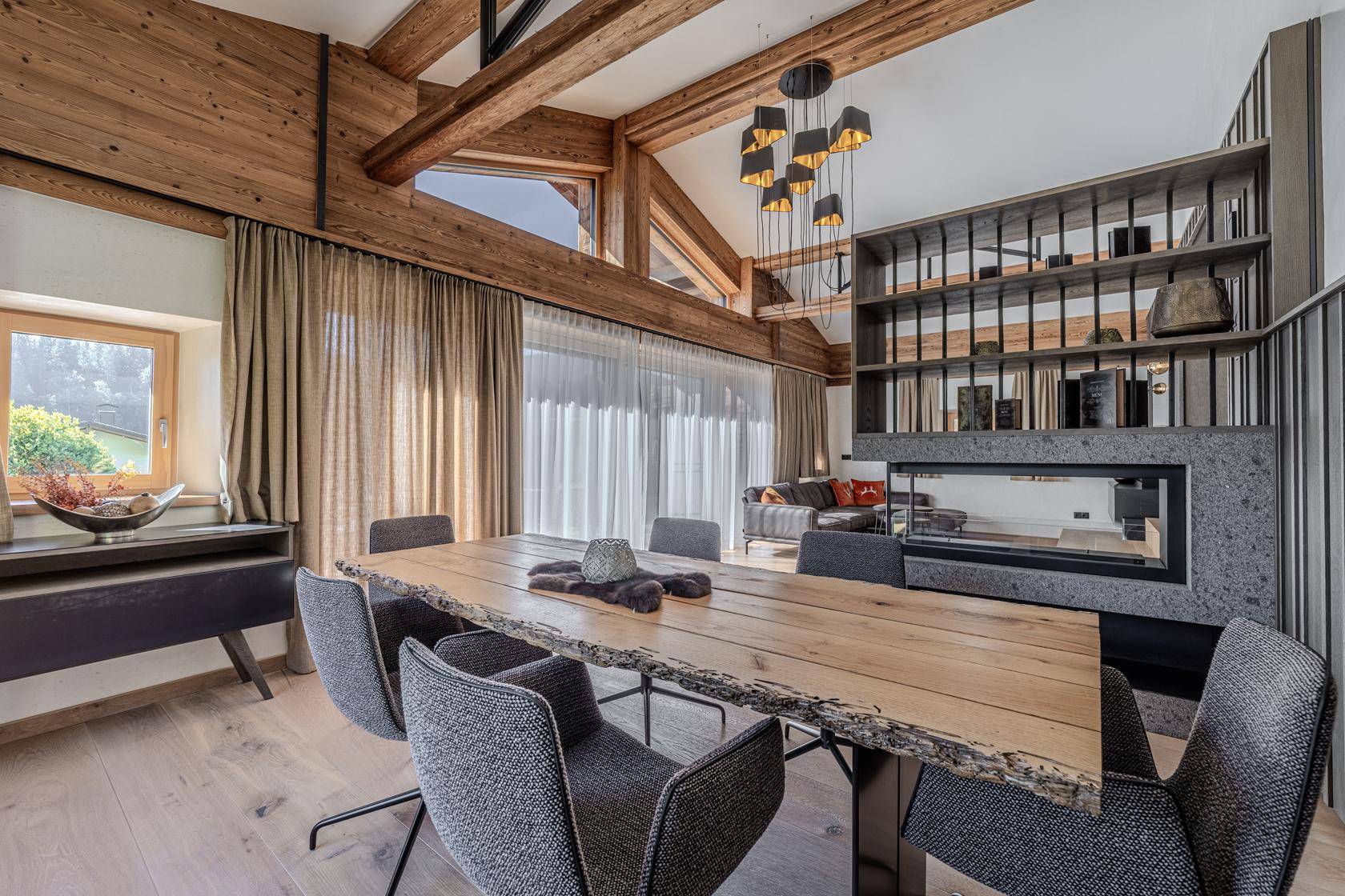 Eleganter Essbereich mit großem Holztisch, modernen Leuchten und Blick auf die Berge.