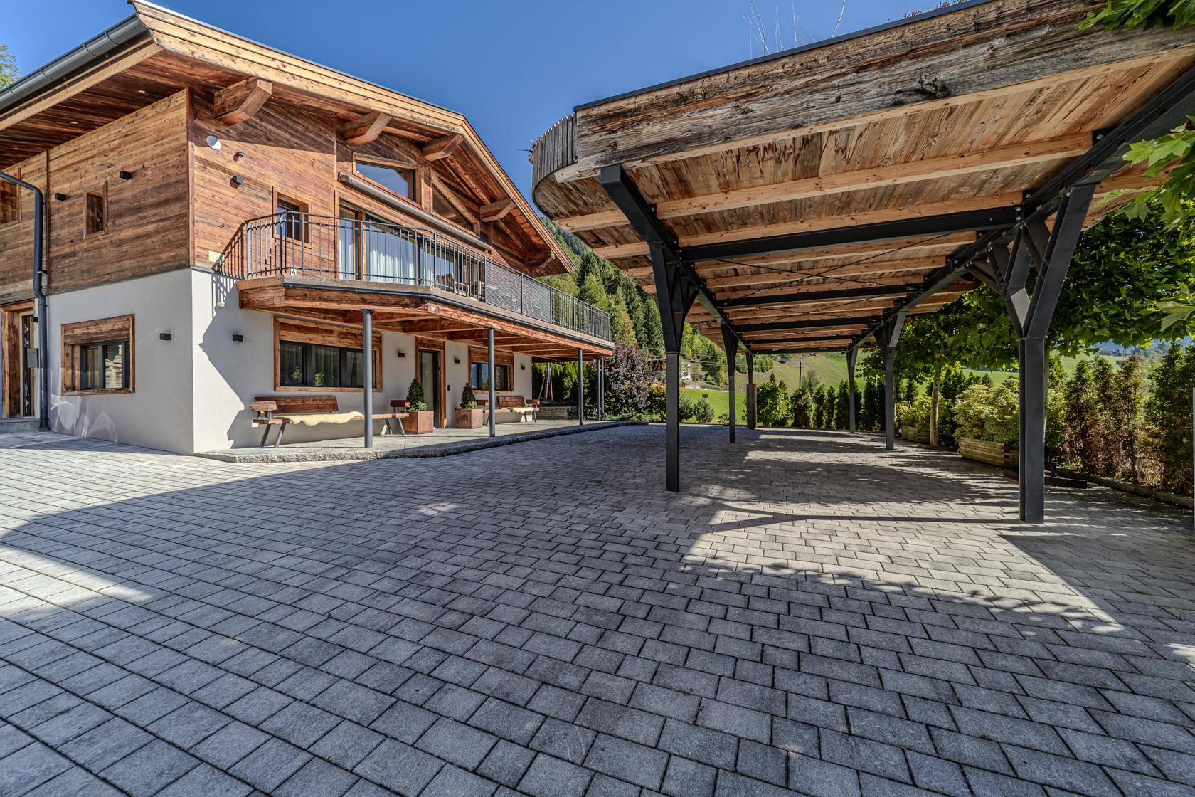 Charmantes Holzhaus mit modernem Carport und gepflasterter Auffahrt in ländlicher Umgebung.