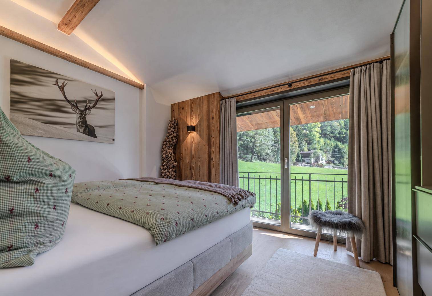 Helles Schlafzimmer mit Holzwand, Balkonzugang und Blick auf die grüne Landschaft.