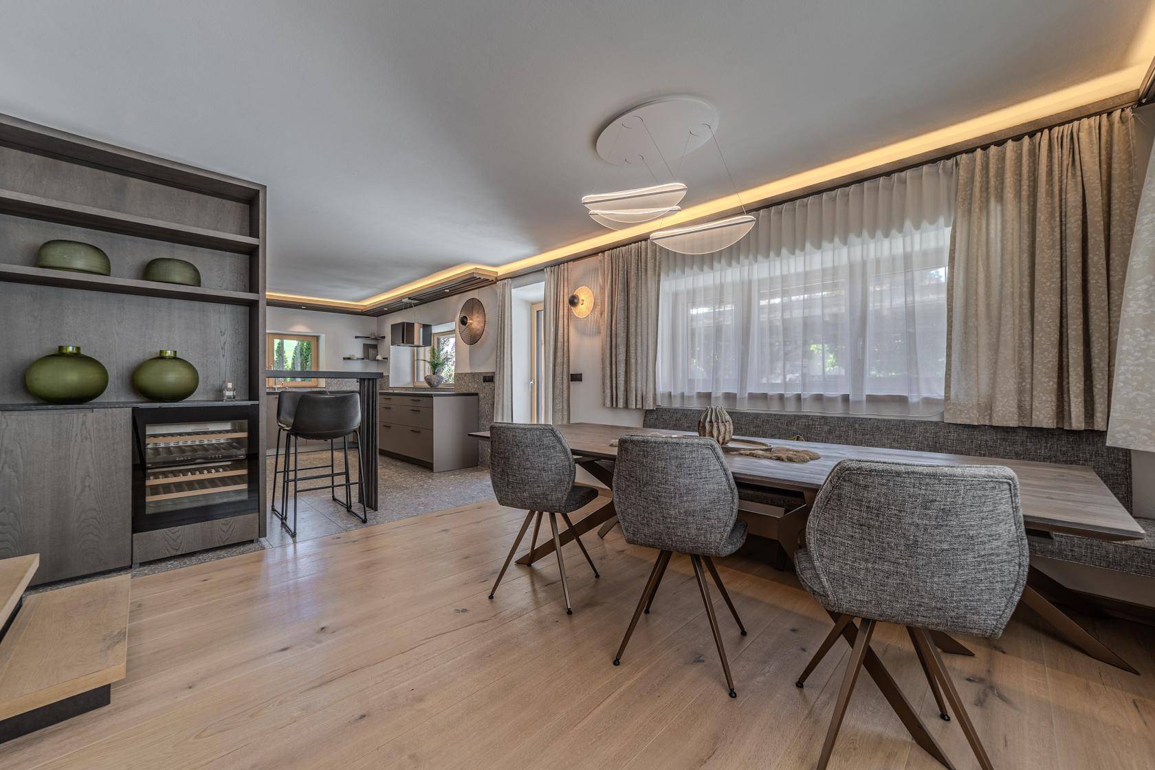 Moderner Essbereich mit Holztisch, integrierter Sitzbank und offener Küche im Hintergrund.