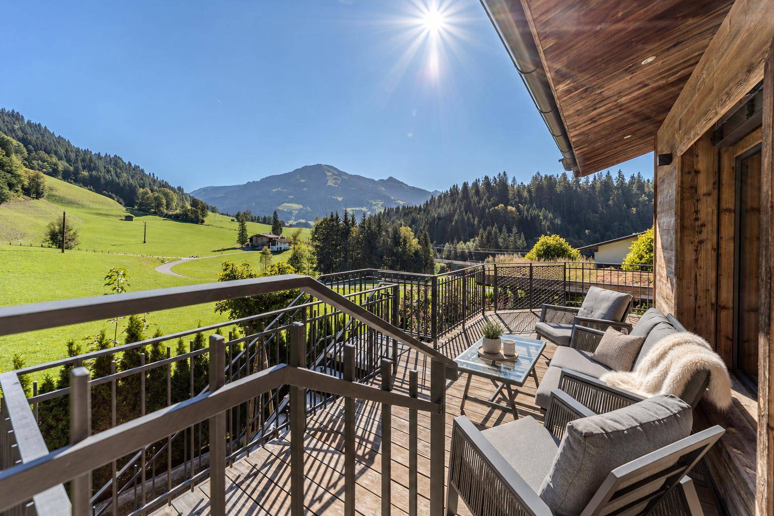 Sonniger Balkon mit bequemen Sitzmöbeln und weitem Blick über die grüne Berglandschaft.