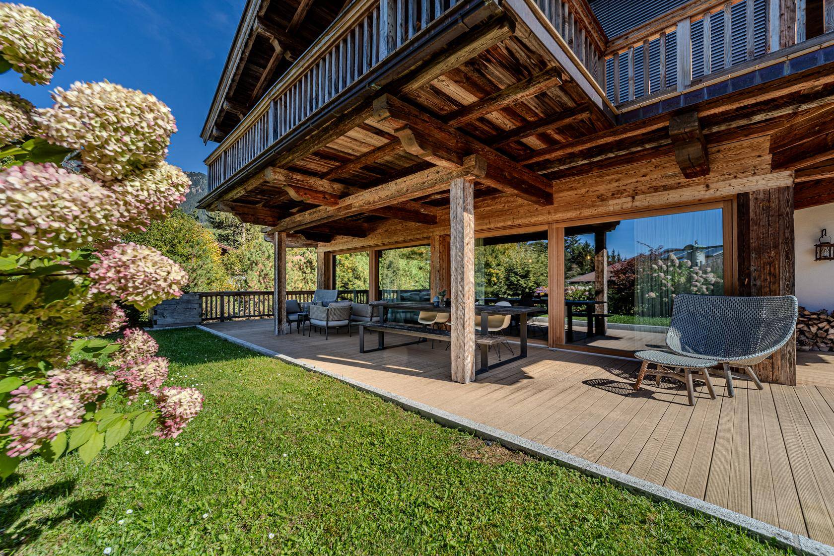 Sonnige Holzterrasse mit Gartenmöbeln und üppiger Bepflanzung am Chalet.