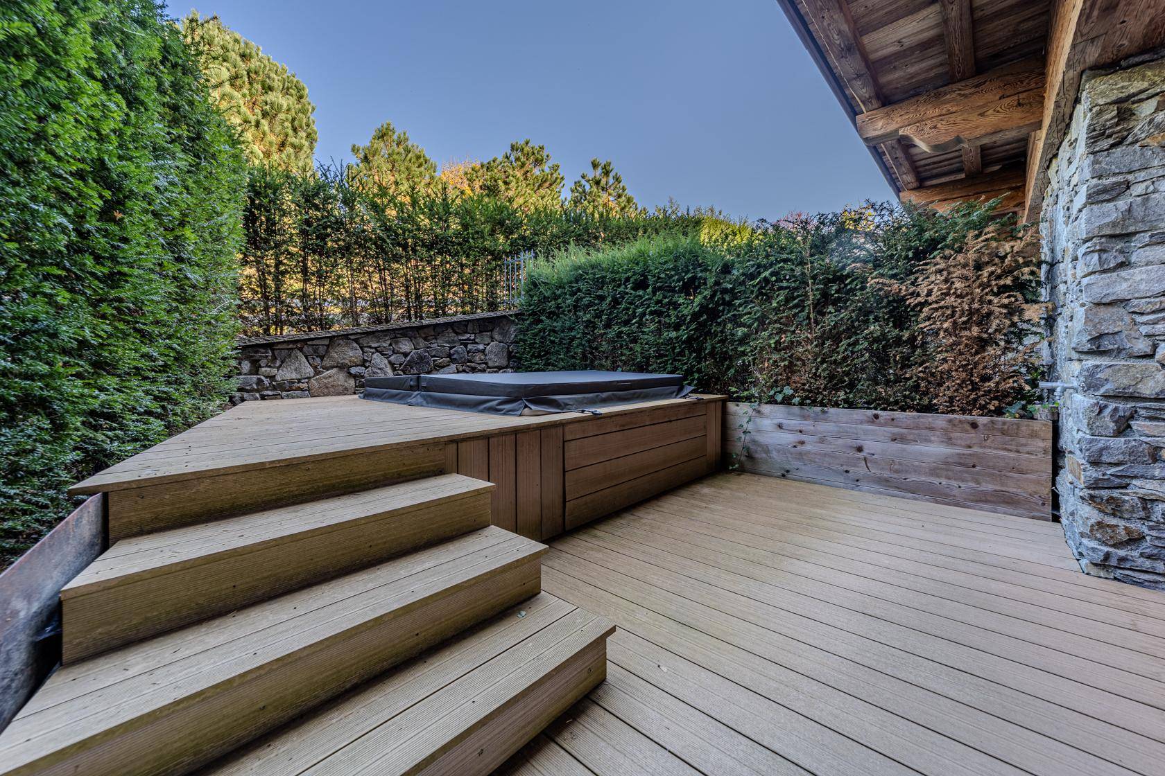 Holzterrasse mit integriertem Whirlpool, umgeben von Hecken und Steinmauern.