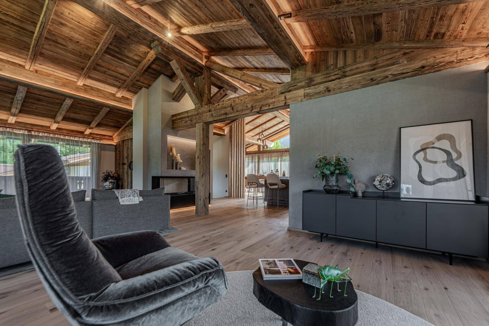 Gemütliches Wohnzimmer mit Holzbalkendecke, modernem Kamin und Blick auf den offenen Küchenbereich.
