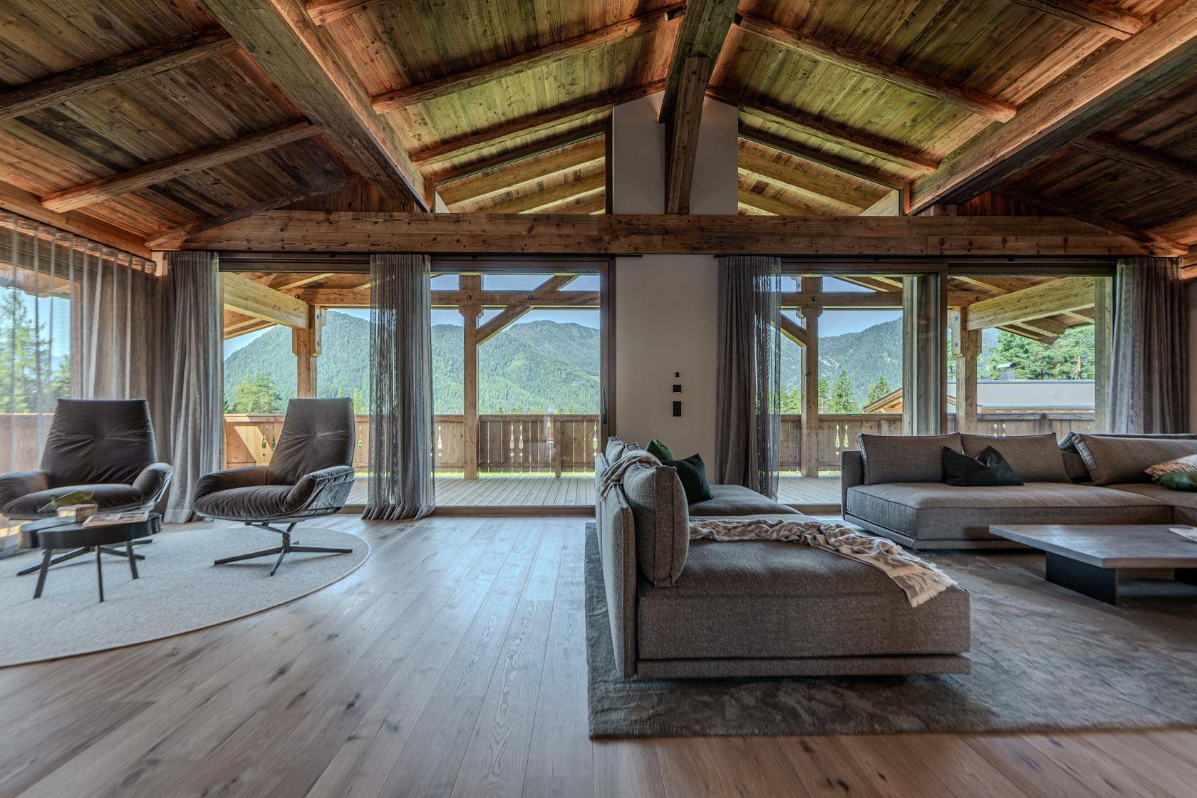 Helles Wohnzimmer mit großen Fenstern, Holzbalkendecke und Zugang zu einem Balkon mit Bergblick.