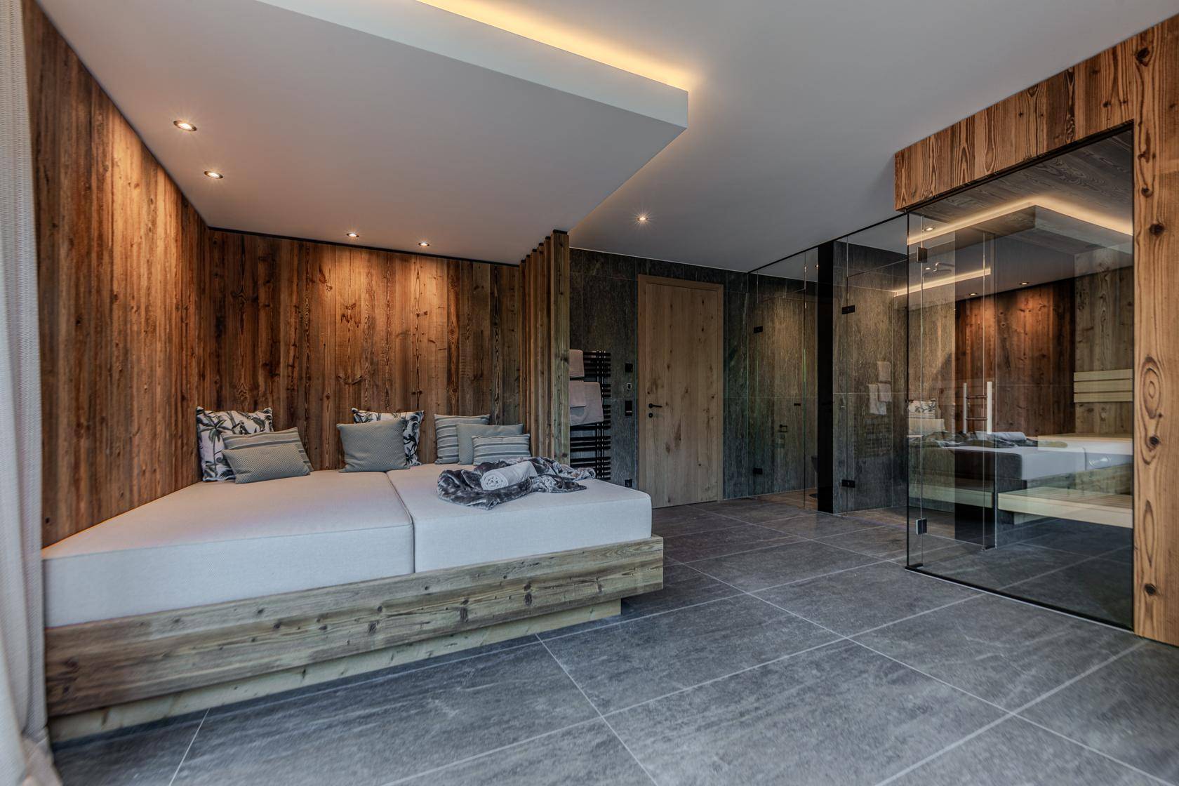 Entspannungsbereich mit Liegefläche und integrierter Sauna, gestaltet mit Holz und Fliesen.
