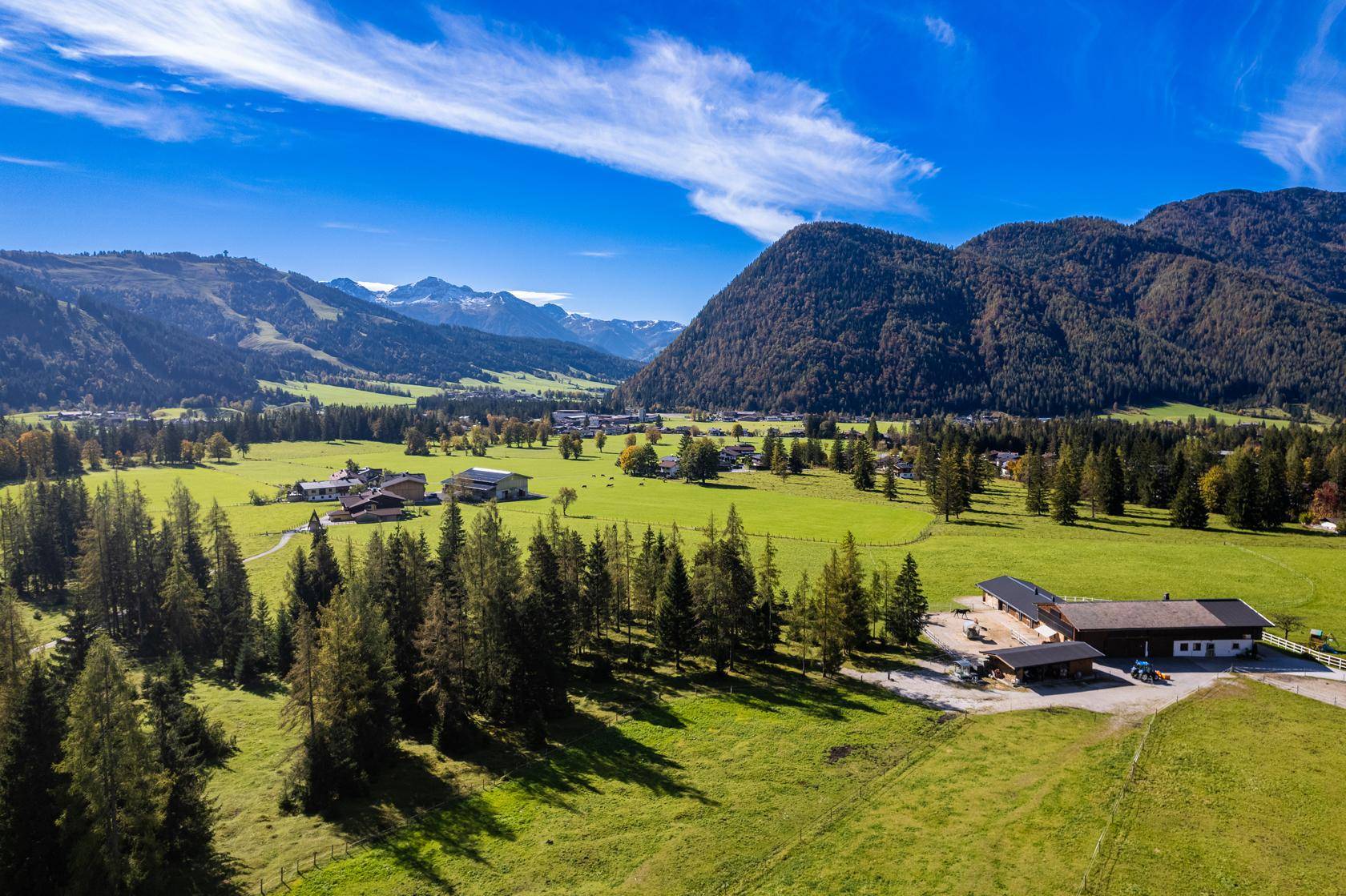 Weitläufige Landschaftsaufnahme eines grünen Tals mit Bergen, Wäldern und vereinzelten Gebäuden.