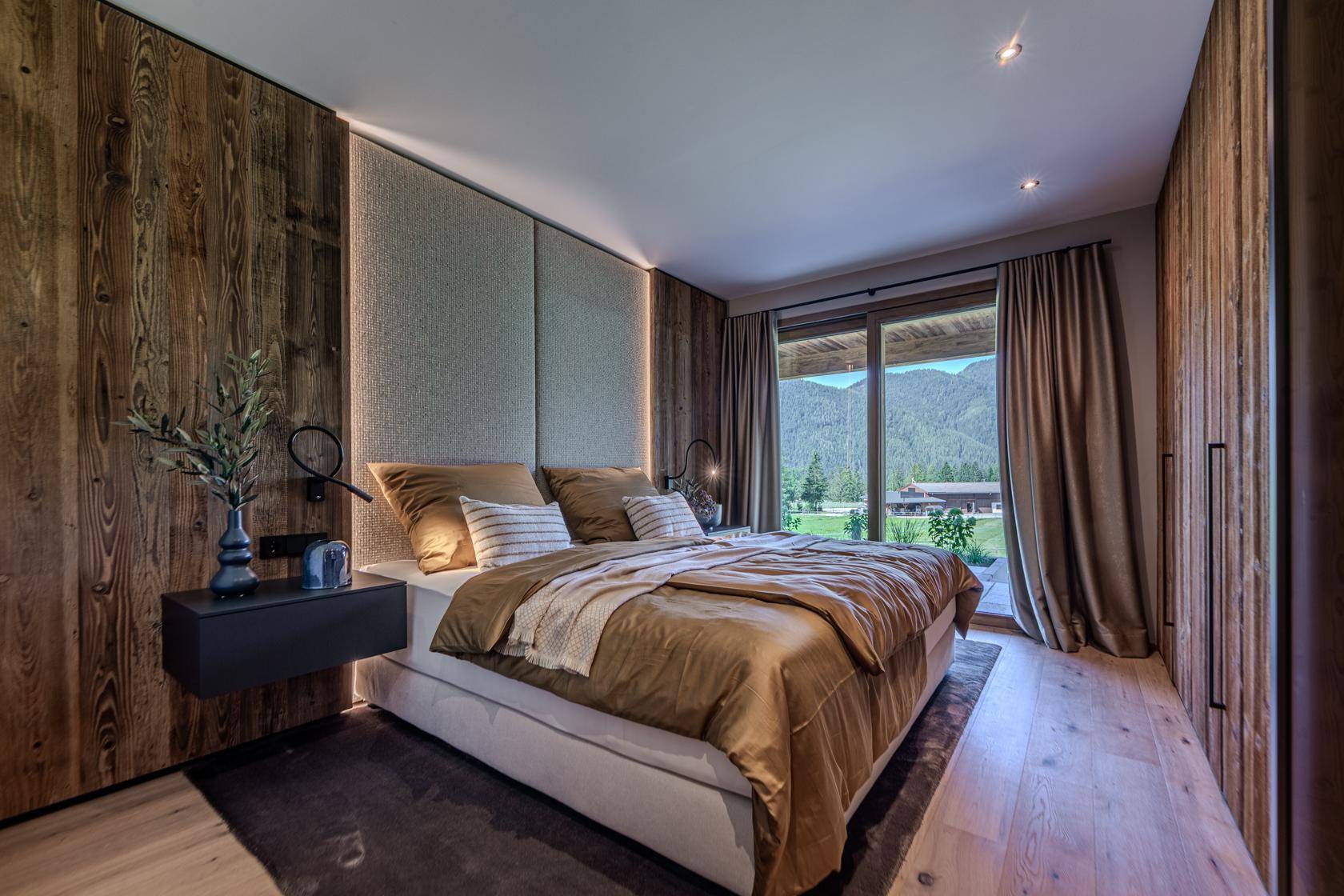 Gemütliches Schlafzimmer mit Holzwänden, großem Bett und direktem Blick auf die umliegenden Berge.