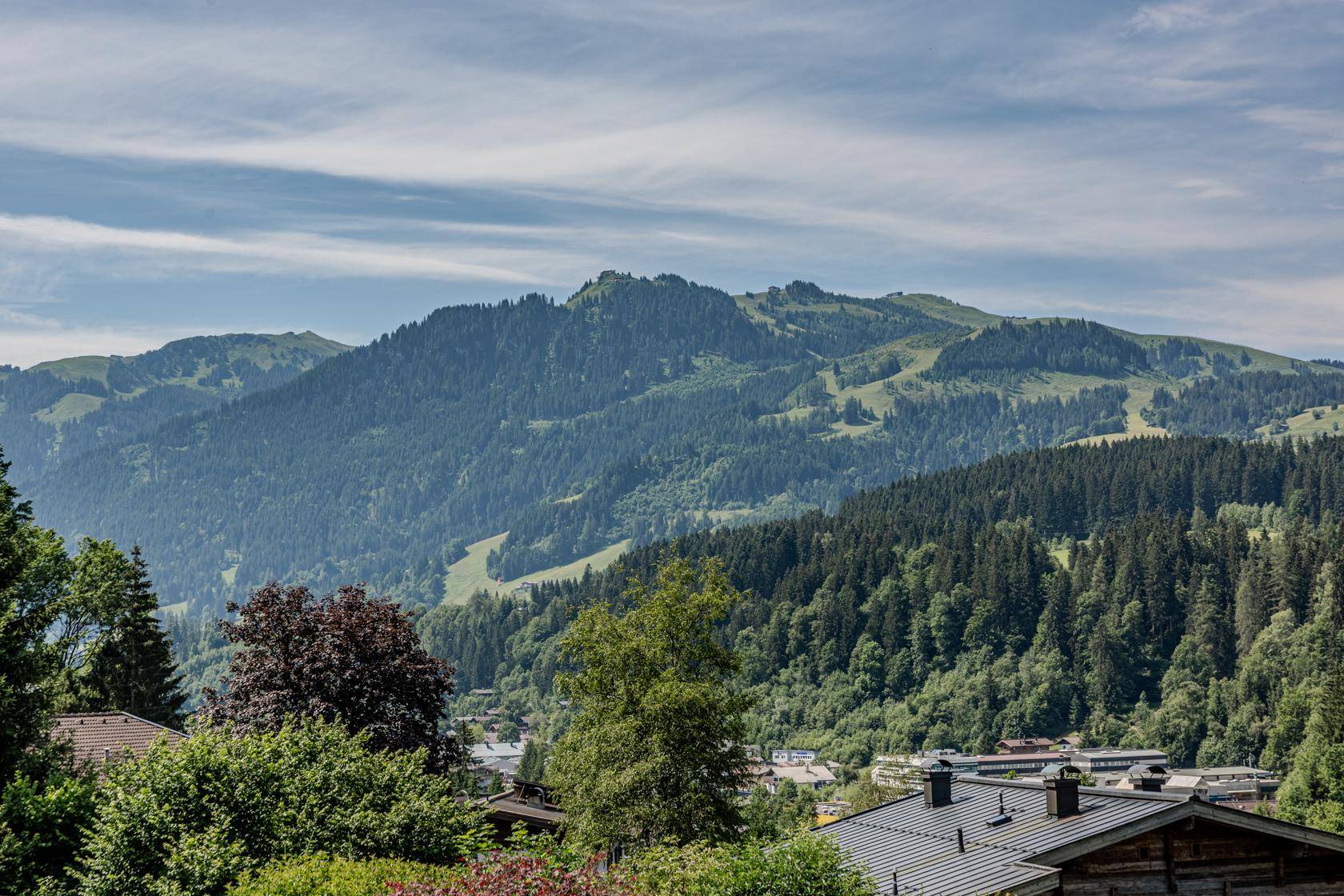 Panoramablick auf bewaldete Berge und eine Siedlung unter einem leicht bewölkten Himmel.