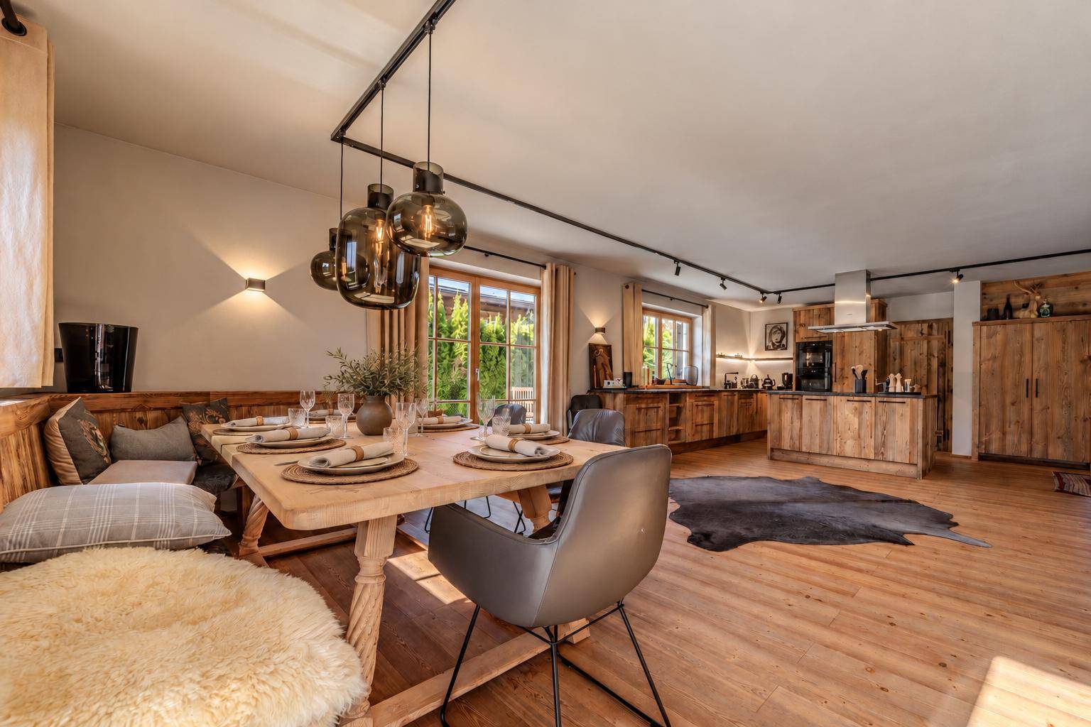 Gemütlicher Essbereich mit Holztisch und Sitzbank, offen zur modernen Holzküche und mit Blick ins Grüne.