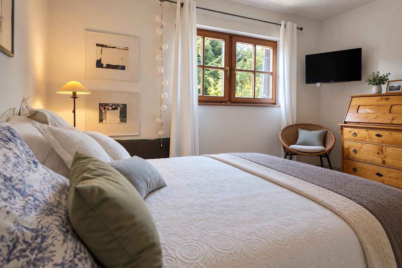 Helles Schlafzimmer mit gemütlichem Bett, Holzkommode und einem Fenster mit Blick ins Grüne.