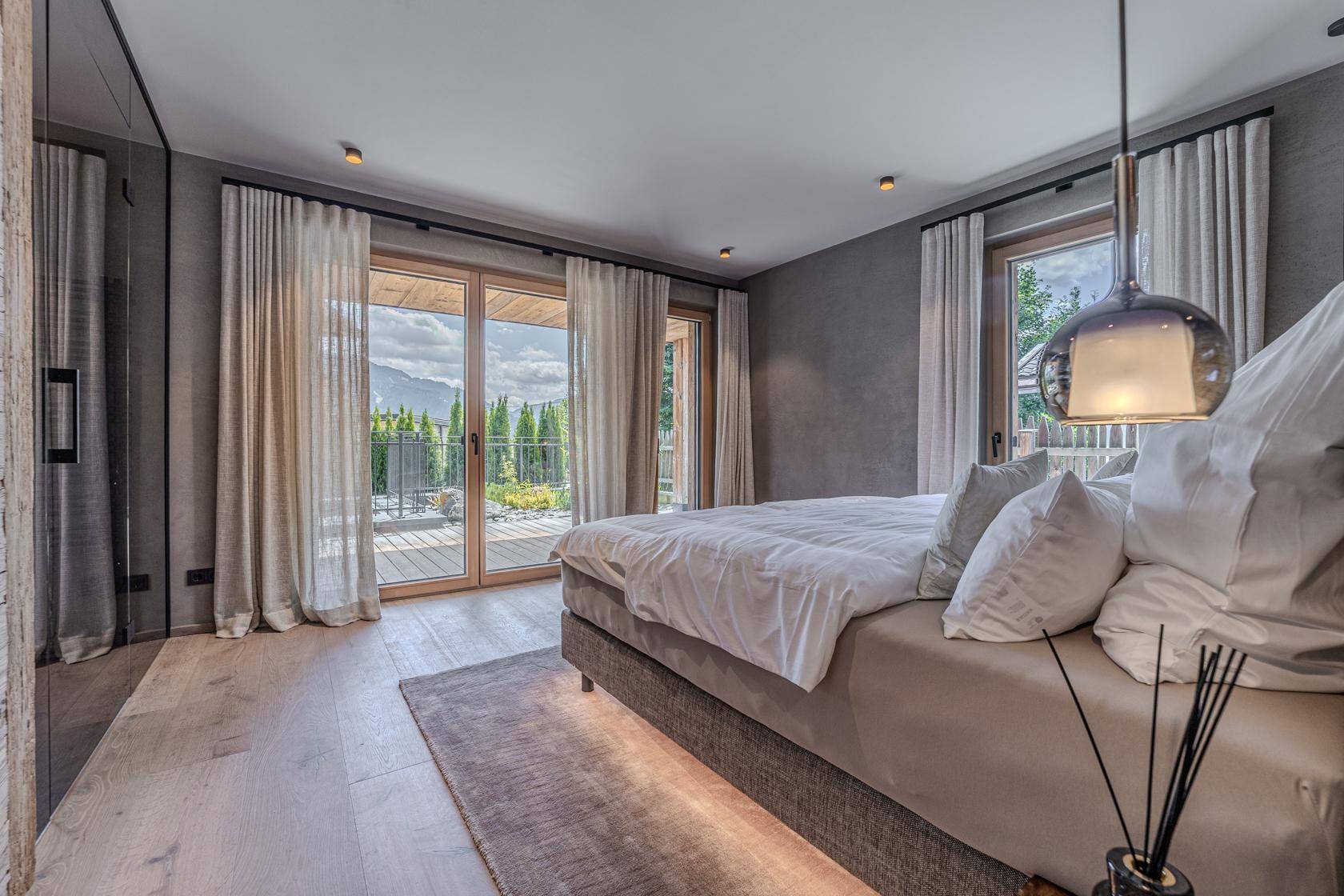 Helles Schlafzimmer mit Doppelbett, Holzboden und Zugang zu einem Balkon mit Bergblick.
