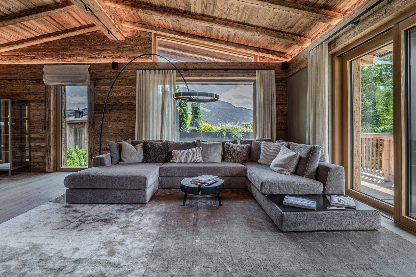 Geräumiges Wohnzimmer mit großem Ecksofa, Teppich und Panoramafenstern mit Bergblick.