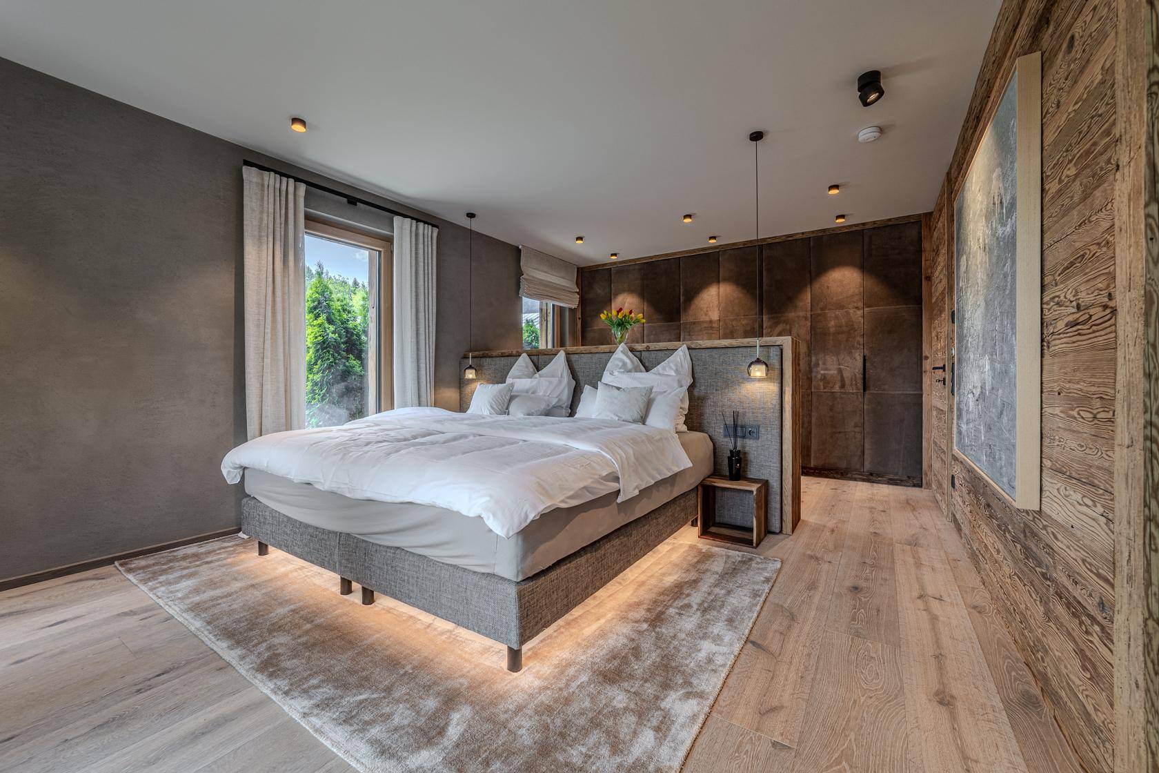 Modernes Schlafzimmer mit großem Bett, Holzwandakzenten und Blick auf die grüne Umgebung.